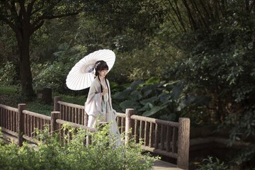 Young woman with umbrella walking on a bridge in nature.