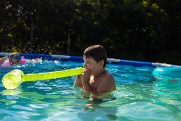 A boy blows up a toy while swimming next to a girl in a colorful backyard pool, enjoying summer days filled with laughter, splashes and playful moments. Children swimming in the pool.