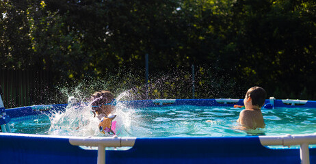 Children Splashing in a Pool - On a sunny summer day, two children enjoy time spent in a backyard pool, splashing and playing with inflatable toys, creating refreshing jets of water.