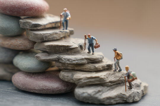 Miniature figures of hikers with backpacks ascending a staircase made of stacked stones, a powerful conceptual metaphor for life's journey, career progress, teamwork, and achieving goals.