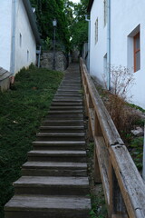 A worn wooden staircase climbs up a historic, stone-paved street, lined with aged buildings and...