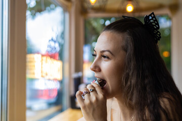 Sitting near the window of a cafe, a young woman savors a moment of indulgence as she thoughtfully...