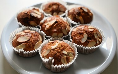 A close-up of freshly baked homemade almond muffins arranged on a white plate. The muffins are golden brown, perfect for breakfast or tea.