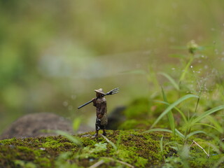 Mini toy of action figure at table with blurred background. Miniature photography concept design. Minifigure of farmer character walking at grass land.