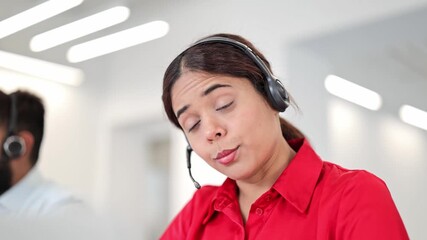 Cheerful Indian woman in red shirt, wearing a headset, actively assists customers in a modern office. Professional female specialist provides excellent, focused customer service.