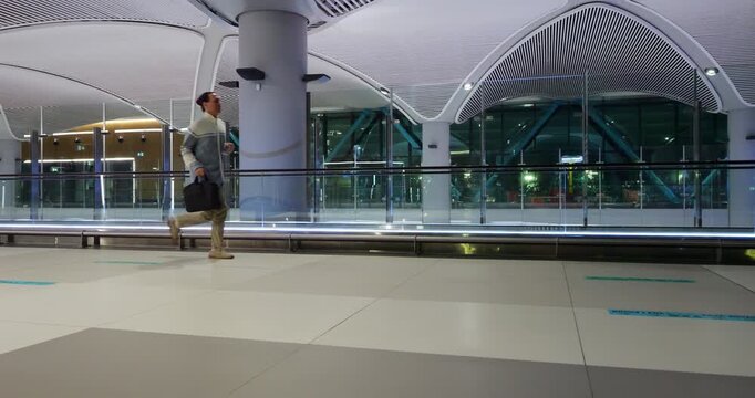 Man seems to be in hurry to connecting flight after first one was arrive late due to delay. Passenger run through big empty terminal with laptop bag, slow motion wide angle shot