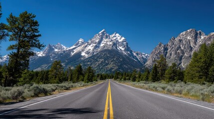Fototapeta premium Road stretches toward majestic snow-capped mountains under a vibrant blue sky