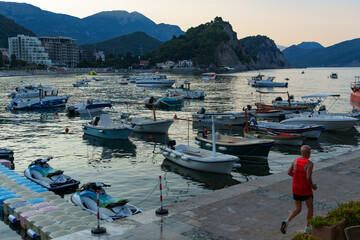 sunrise on adriatic sea coast, petrovac city in early morning, an elderly man on a morning jog,...