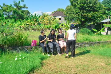 As three girls are already seated, one adjusts her position to join them on a grassy edge amid...