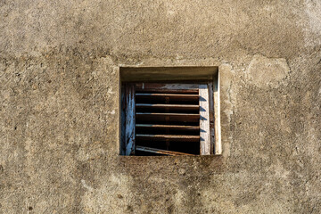 old weathered plaster wall with small ventilation window with wooden blinds