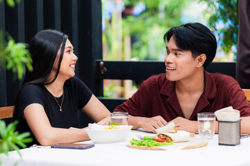 Playful young Asian couple enjoy a lively chat during their lunch date at an alfresco cafe.