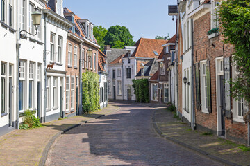 Obraz premium A charming, winding cobblestone street in Amersfoort, lined with traditional Dutch houses in varying colors, under a clear blue sky.