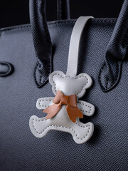 Close-up of a gray leather bag charm in the shape of a cute bear on a  black bag