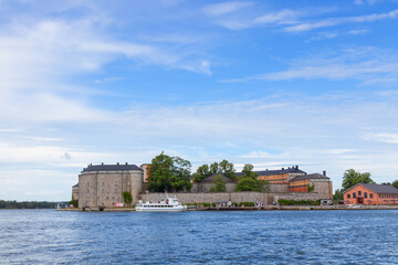 The historic stone Vaxholm Fortress stands surrounded by water and lush greenery, with a Swedish flag flying proudly atop its walls, rich heritage and scenic coastal location