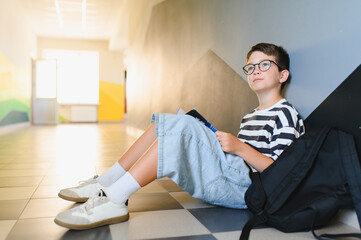 Thoughtful student reading a book in school hallway