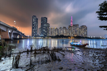 Naklejka premium Modern skyline of Ho Chi Minh City viewed across Saigon river, showcasing high-rise buildings reflecting the city's rapid urban development.