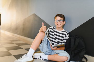 Smiling student reading book showing thumbs up in school corridor