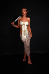 Slender young woman in white cloth holding traditional indian sword low key full length portrait