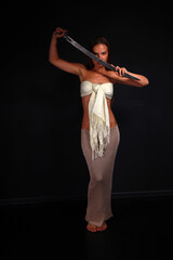 Fototapeta premium Slender young woman in white cloth holding traditional indian sword low key full length portrait