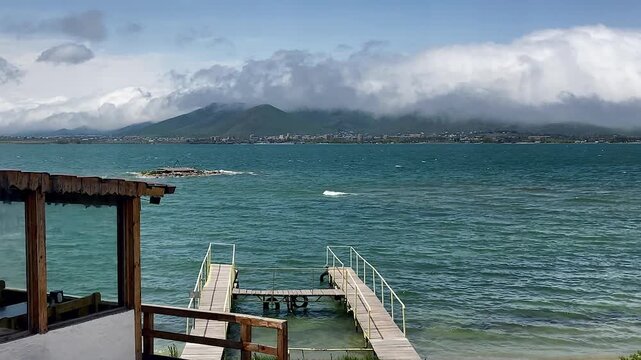 Dramatic view at lake with big clouds, pier leading into water. Sevan, Armenia