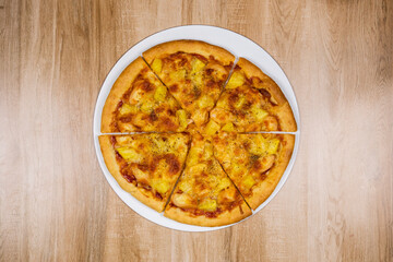 Top view of delicious and crispy hawaiian pizza topping with mozzarella cheese, pineapple and tomato source on wooden texture table background.