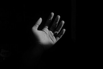 A human hand is illuminated by sunlight in the midst of darkness. The high contrast between light...