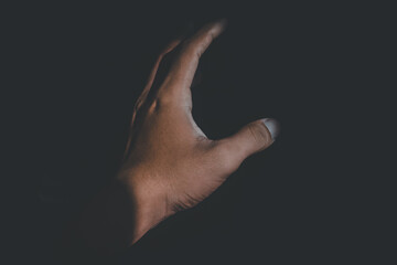 A human hand is illuminated by sunlight in the midst of darkness. The high contrast between light...