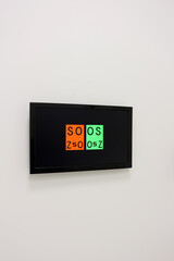 Digital vision testing screen mounted on a white wall, displaying optometric symbols in red and...