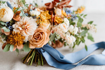 Rustic wedding bouquet with warm-toned florals and greenery, tied with an elegant blue ribbon