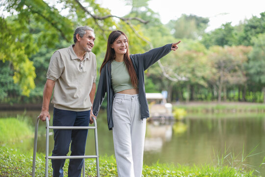 elderly man using walker aid rehabilitation in the park with a young adult daughter take care and support