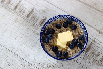 Bowl of oatmeal with butter and blueberries on wooden background. Healthy food concept
