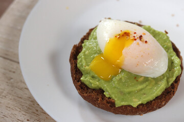 Avocado toast with poached egg and spices on a white plate