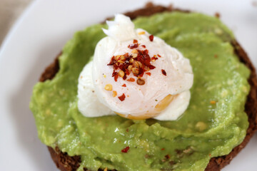 Avocado toast with poached egg and spices on a white plate