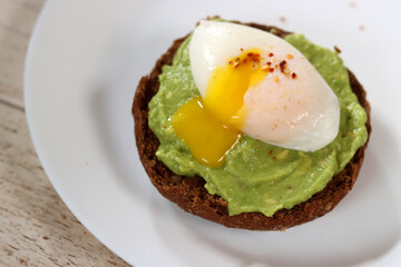 Avocado toast with poached egg and spices on a white plate