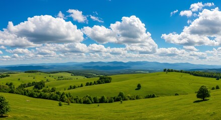 Obraz premium Panoramic Landscape of Lush Green Rolling Hills, Bright Blue Sky with Fluffy White Clouds, Scenic View of Mountains and Trees in the Distance