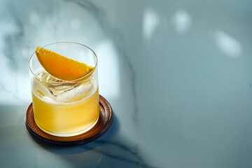 an orange clear color cocktail liquor serving with sliced orange in old fashioned glass put on white marble table
