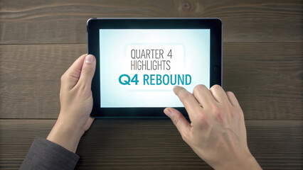 Person interacts with tablet displaying Quarter 4 Highlights Q4 Rebound on wooden table. Q4 Rebound