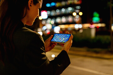 Modern urban female checking GPS map on smartphone outdoors at night