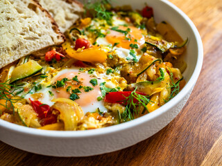 Shakshuka - fried eggs with vegetables and bread on wooden table	