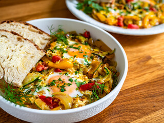 Shakshuka - fried eggs with vegetables and bread on wooden table	