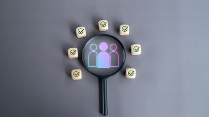Fototapeta premium Magnifying glass highlighting a group of people icon surrounded by checkmark blocks on a gray background. Concept of HR recruitment, team selection, and talent matching.