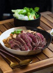 A plate of fried rice topped with sliced beefsteak. Steak bowl is a dish in which a meat is grilled, cut into bite-sized pieces, placed on top of rice in a bowl, and topped with sauce