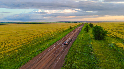 a car on a country road in a wheat field at sunset
