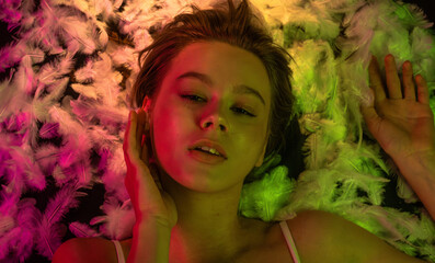 Top view of young woman with neon lighting and feathers in beauty concept
