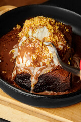 Fork digging into warm chocolate brownie with vanilla ice cream and cookie crumbles