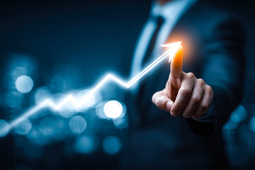 Business professional pointing at an illuminated upward trending graph representing growth and success