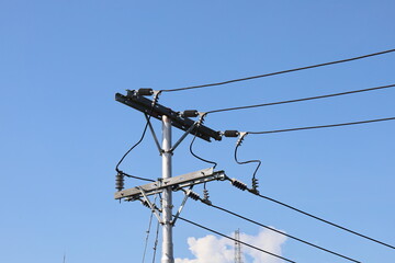 High-voltage power lines crisscross the blue sky, supported by massive industrial pylons and towers...