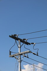 High-voltage power lines crisscross the blue sky, supported by massive industrial pylons and towers that deliver electricity