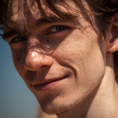 Obraz premium Side profile portrait of a smiling 25-year-old skinny Caucasian male model with neat hair and clear skin, under vibrant sunny daylight.