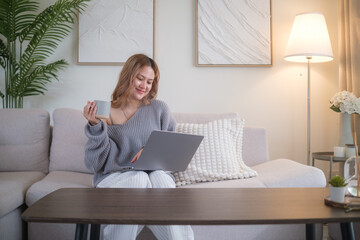 Smiling young woman working on a laptop with a coffee mug in hand, sitting comfortably on a modern...